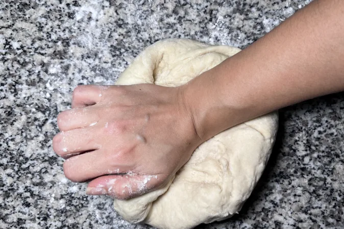 A hand kneading bread dough on a kitchen surface.