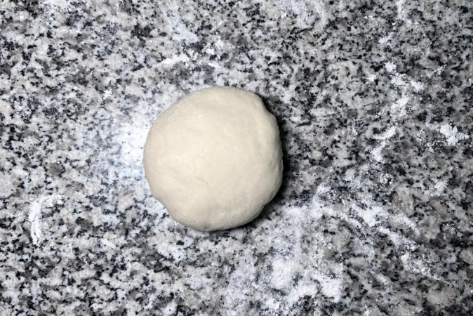 A ball of bread dough on a floured kitchen surface.