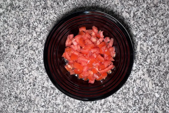 A black bowl full of chopped tomatoes.