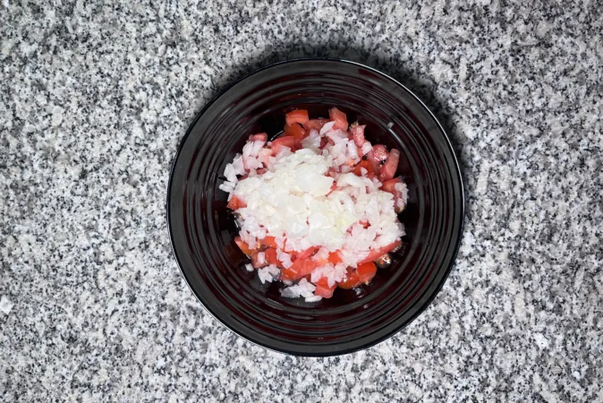 A black bowl full of chopped tomatoes and onion.