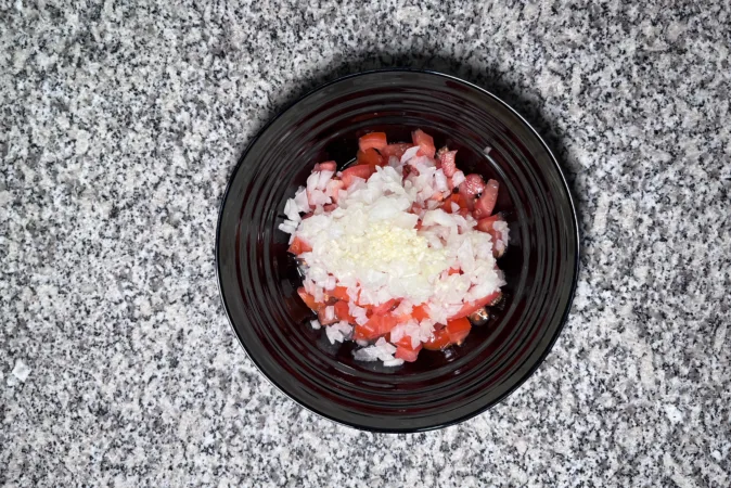 A black bowl full of chopped tomatoes, onion and garlic.