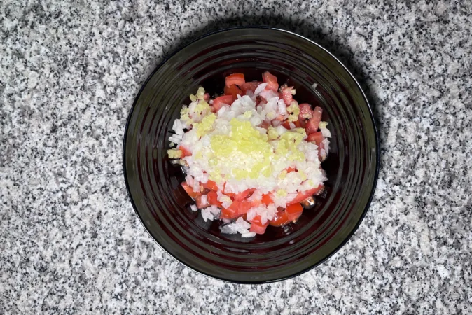 A black bowl full of chopped tomatoes, onion, chilli and garlic.