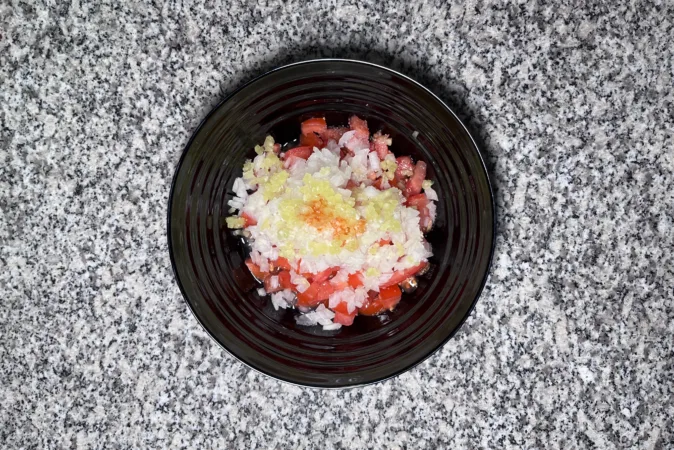 A black bowl full of chopped tomatoes, onion, chilli, garlic and hot sauce.