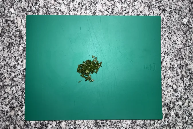 Chopped basil leaves on a green chopping board.