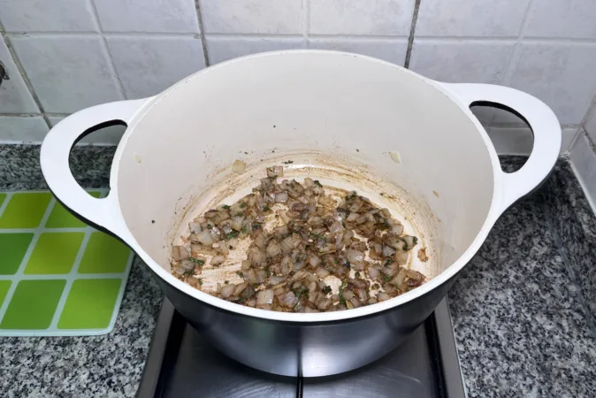 Onion, basil and spices frying in a large soup pan.