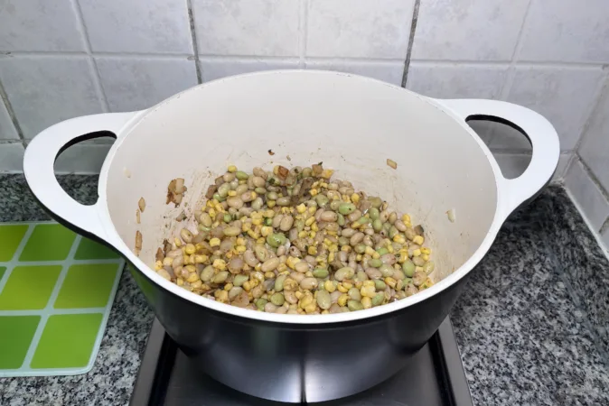 Onion, beans, and corn frying in a large soup pan.