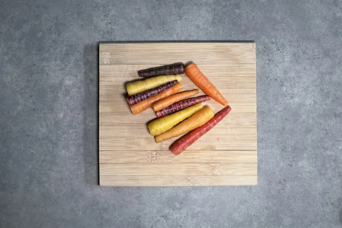 A pile of colourful baby carrots on a wooden chopping board.