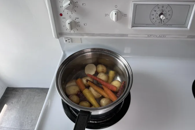 A pan of colourful carrots and new potatoes sit on a hob.