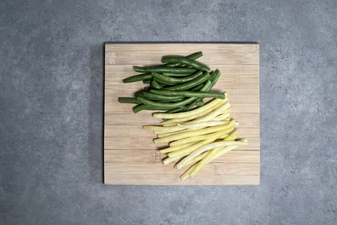 A pile of green beans and a pile of yellow beans sit side-by-side on a wooden chopping board.