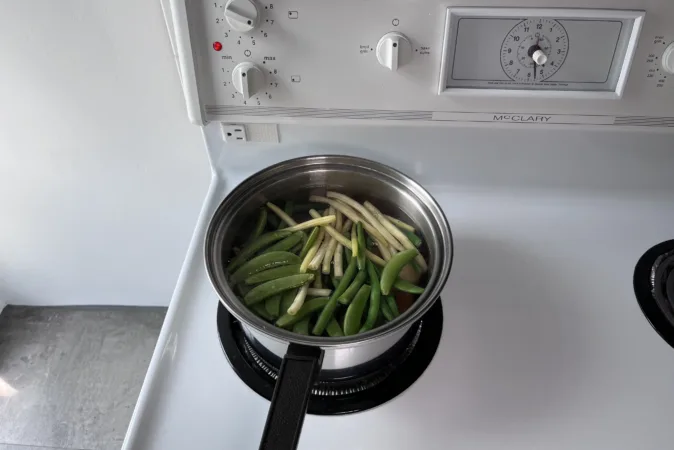 A pan of beans and sugar snap peas on a hob.