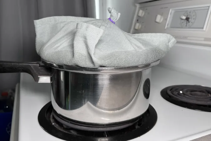 A metal saucepan sits on a hob. The lid is wrapped in a light blue tea towel.