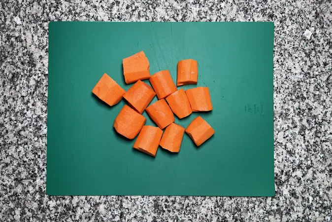 Large chunks of peeled carrots on a green chopping board.