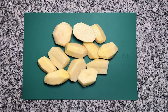 Large chunks of peeled potatoes on a green chopping board.