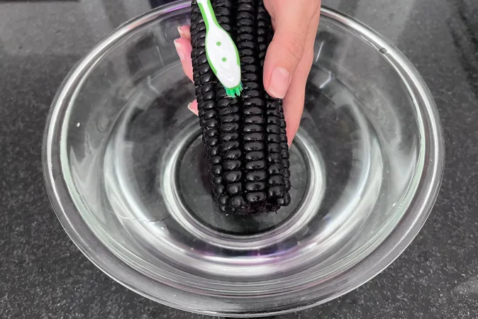 Peruvian purple corn being washed with a toothbrush over a bowl of water.