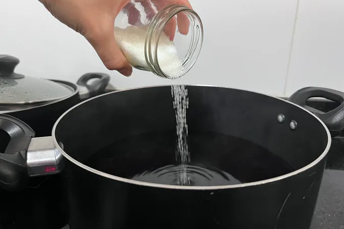 Sugar being poured into a saucepan from a glass jar.