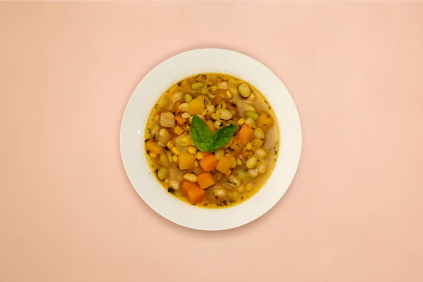 A white bowl full of Porotos Granados, a Chilean bean stew. It sits on a pink background.